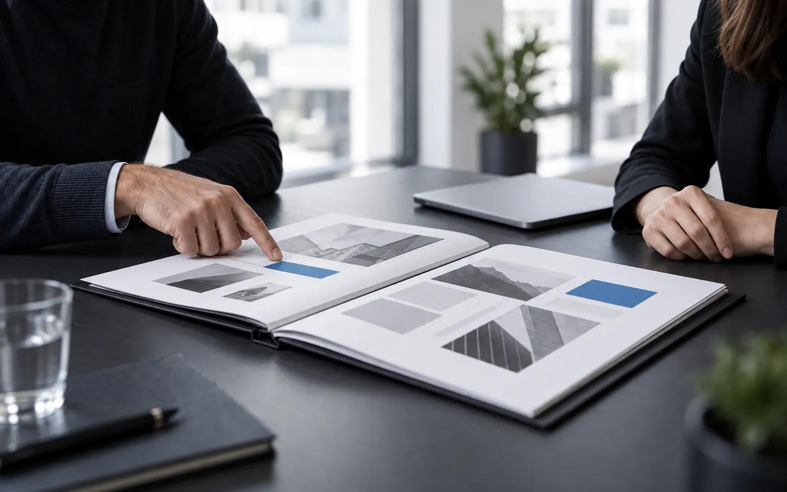 Deux personnes examinent des propositions de mise en page dans un portfolio ouvert sur une table de réunion.